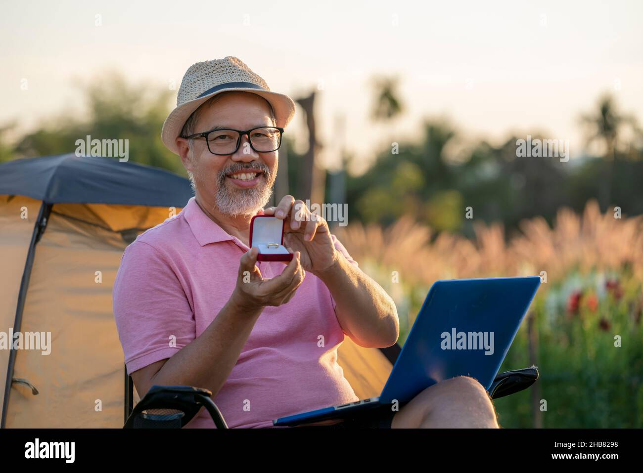 Happiness Man sorpresa matrimonio proposta online per ragazza online attraverso il computer portatile. Pensione barba grigia matura o uomo anziano in rosa e cappello Foto Stock