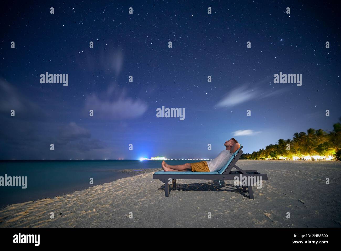 Uomo sdraiato sul lettino sulla spiaggia di sabbia e guardando fino alle stelle sul cielo notturno. Foto Stock