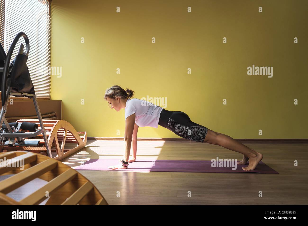 Una donna che pratica yoga, esegue l'esercizio kumbhakasana, posa in asse, treni in studio su un tappeto vicino alla finestra Foto Stock