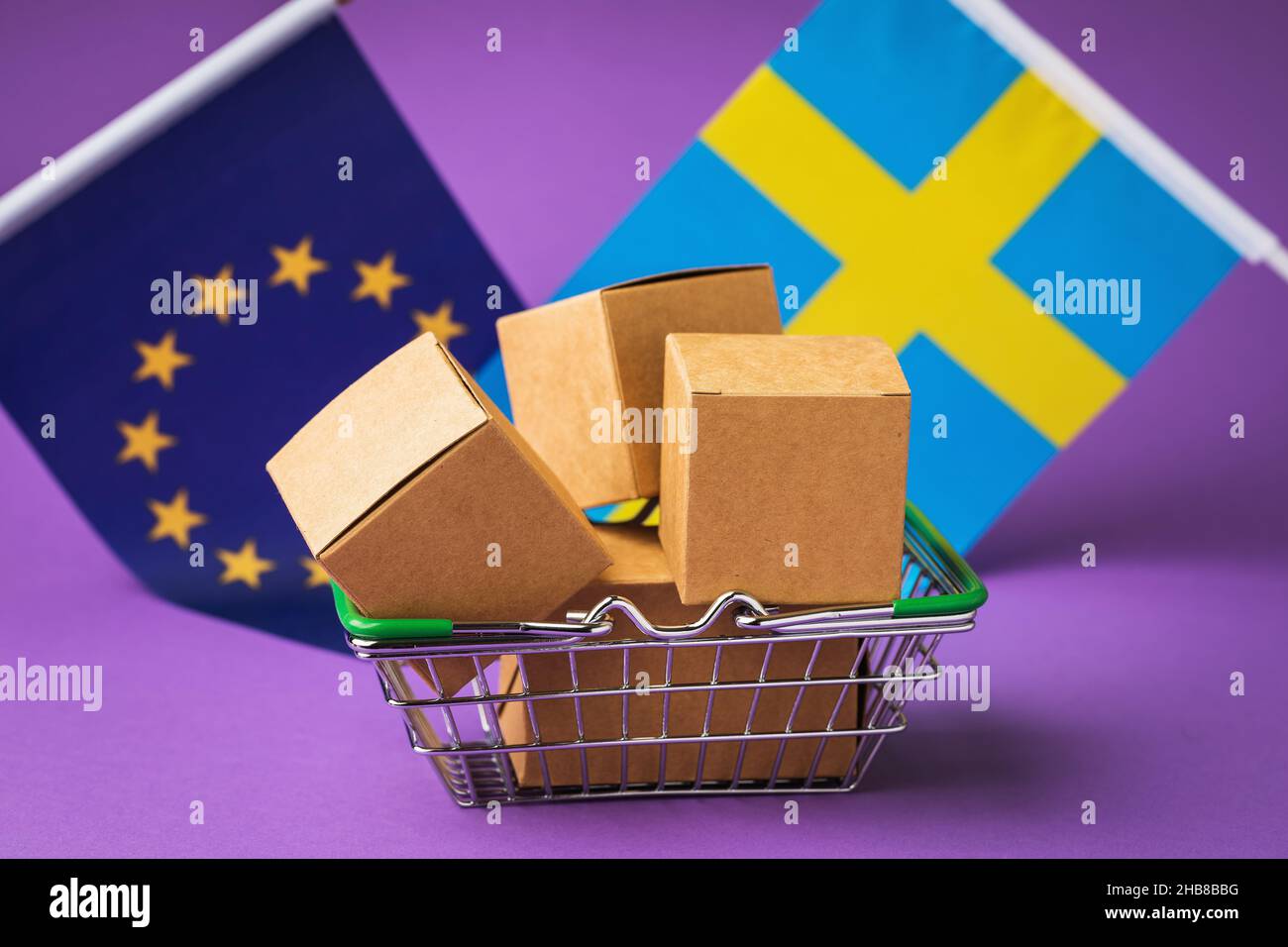 Scatole di cartone in un cestino alimentare e bandiere su sfondo colorato, il concetto di distribuzione di merci svedesi nell'Unione europea Foto Stock