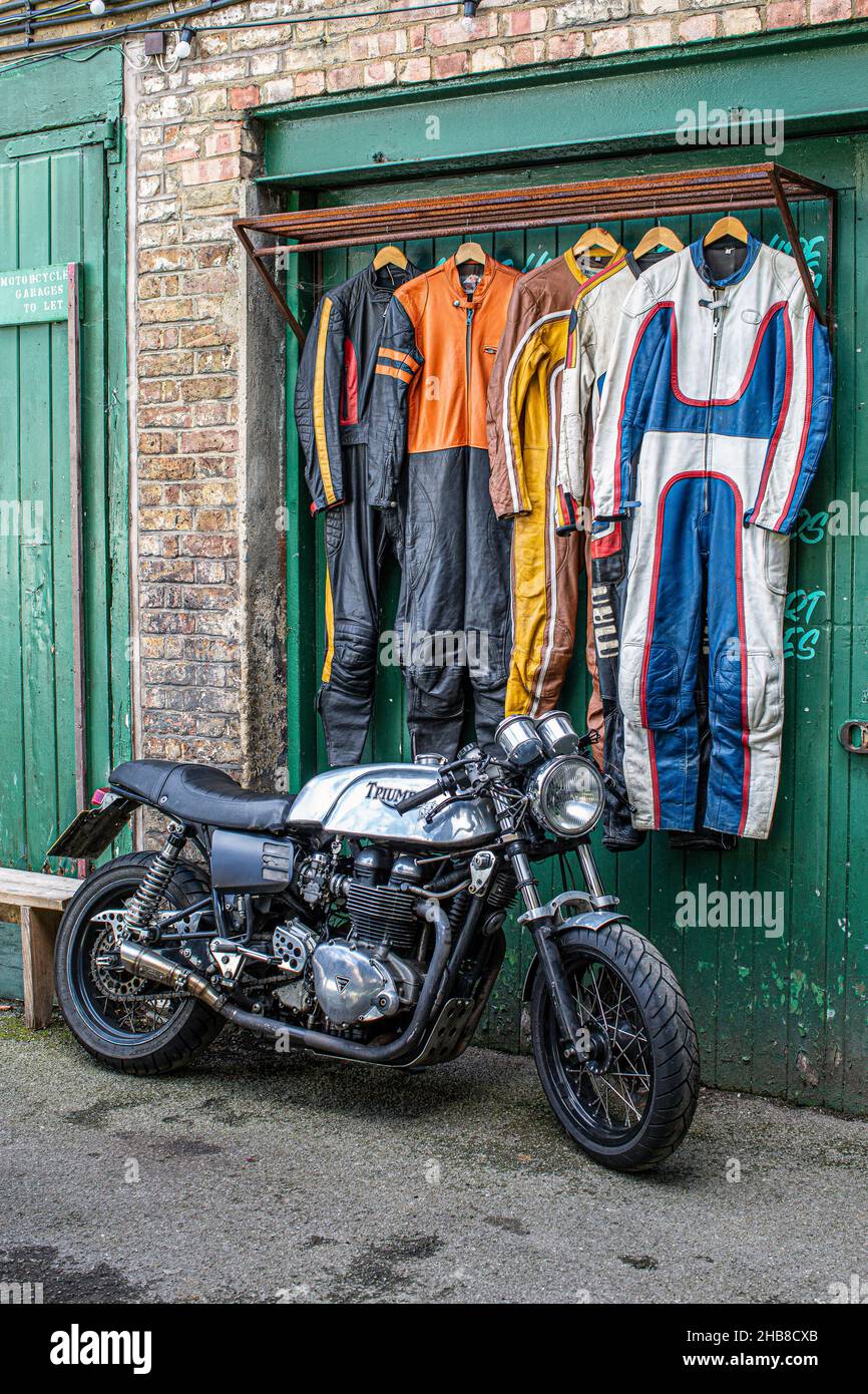 Garage per motociclette con cafè racer e abiti in pelle per motociclette appesi alla parete posteriore. Foto Stock
