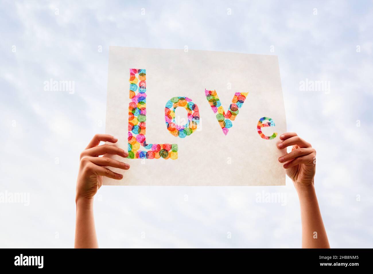 Mano di ragazzo (8-9) tenendo colorato segno di Amore contro il cielo Foto Stock