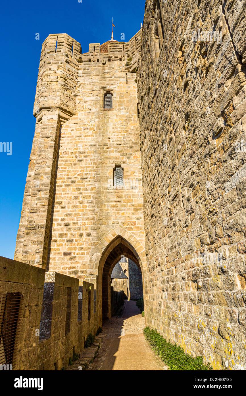 La vista attraverso un portale gotico ad arco appuntito nel muro della Cité de Carcassonne, dipartimento dell'Aude, Francia, si apre su una piazza, una torre merlata – probabilmente la Tour Pinte, la torre più alta dello Château Comtal, la cui muratura più antica è attribuita a origini saracene altomedievali. Foto Stock