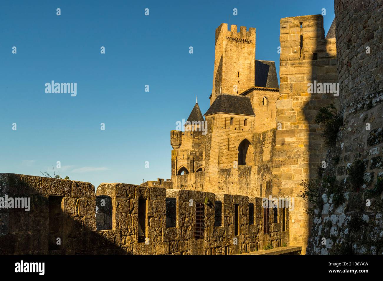 Una torre difensiva quadrata – probabilmente la Tour Pinte, la torre più alta dello Château Comtal, la cui muratura più antica è attribuita a origini saracene altomedievali – si erge nella luce della sera sopra il muro merlato della Cité de Carcassonne, dipartimento dell'Aude, Francia; in primo piano, il camminamento delle mura conduce verso di essa. Foto Stock
