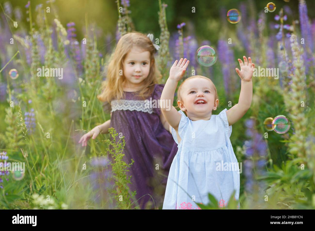 Cute, ragazze piccole in abiti cercare di prendere le bolle di sapone. Divertenti bambini sorridenti sul campo. I bambini giocano all'aperto. Concetto di infanzia felice, amicishi Foto Stock