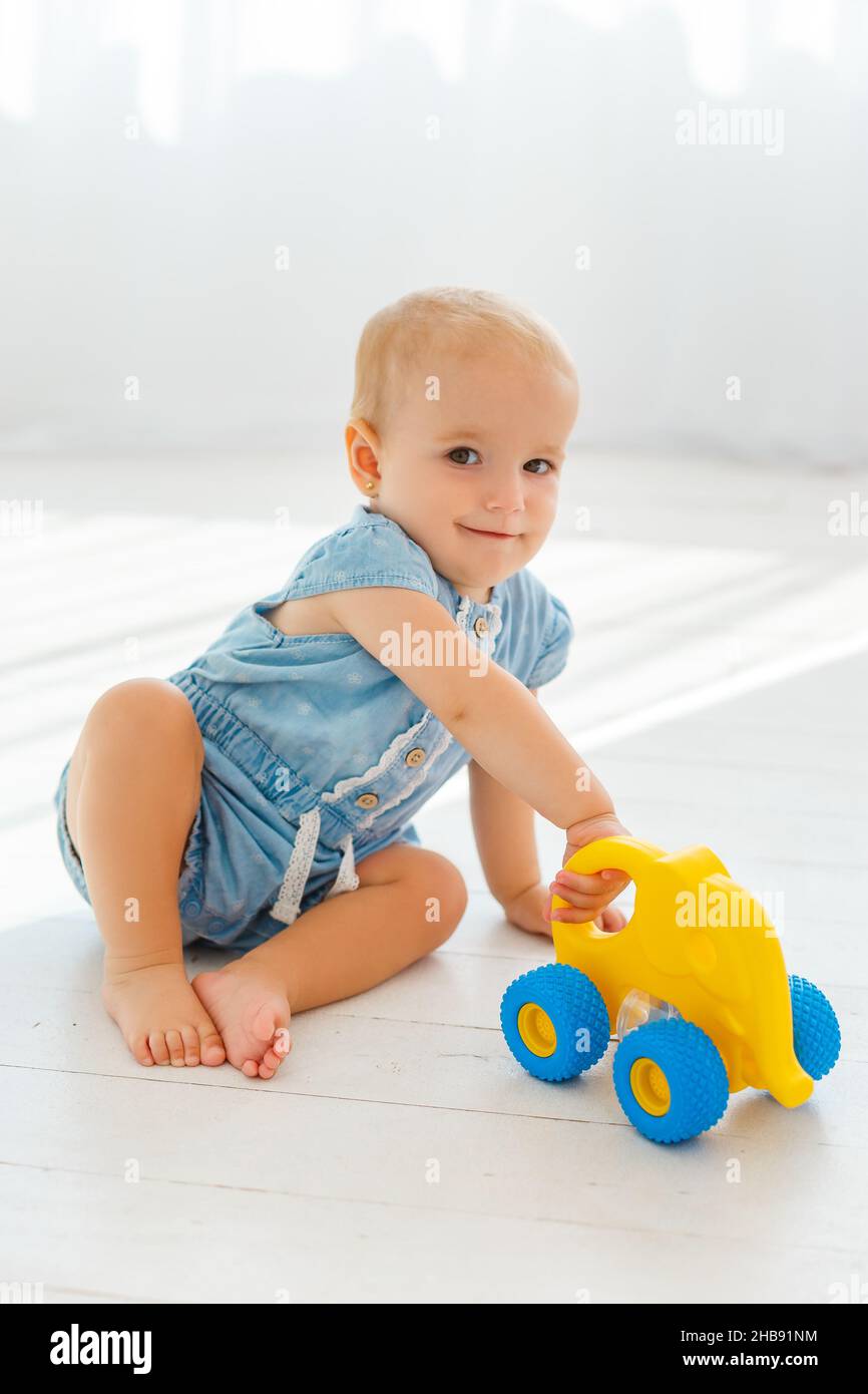 Сute bambina in jeans blu che gioca con elefante giallo. Piccolo toddler sorridente e giocattolo rotolante sul piano.concetto di sviluppo del bambino e felice Foto Stock