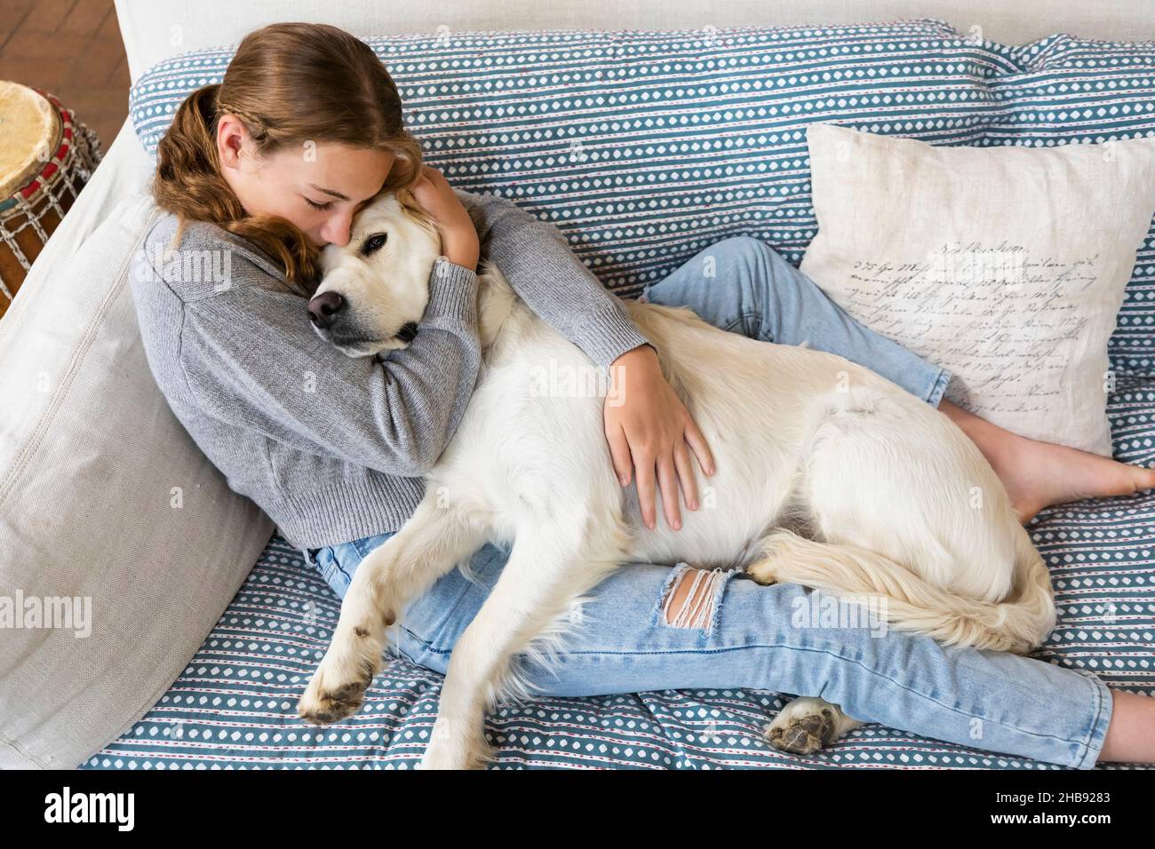 Ragazza (14-15) che abbraccia English Cream Golden Retriever sul divano Foto Stock