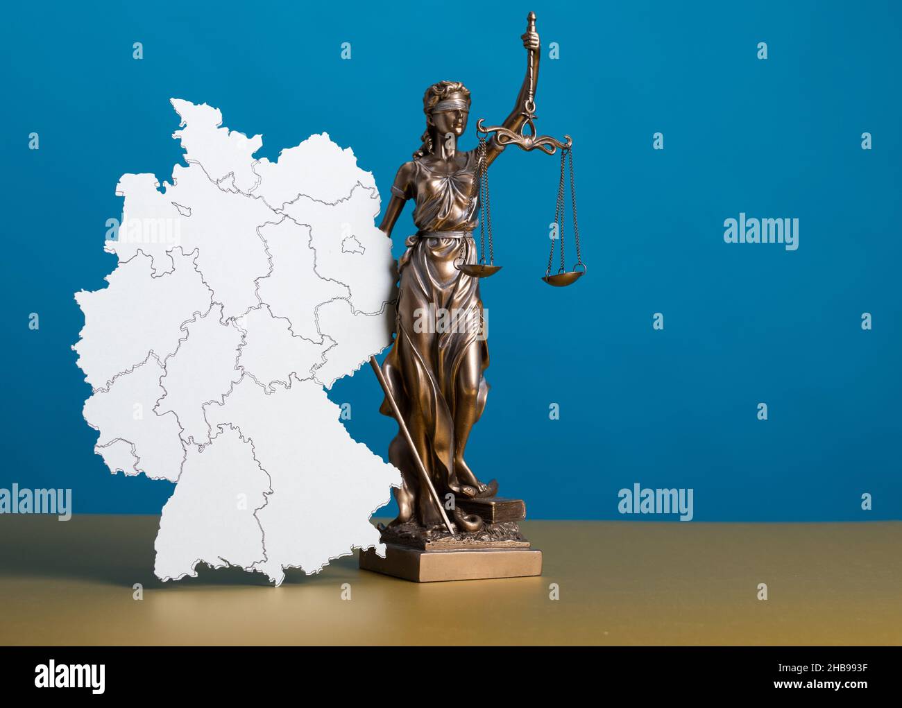 Statua di una donna con scale come simbolo di giustizia su una superficie blu con una sagoma di una mappa Foto Stock Statua di una donna con scale come simbolo di giustizia su una superficie blu con una sagoma di una mappa Foto Stock
