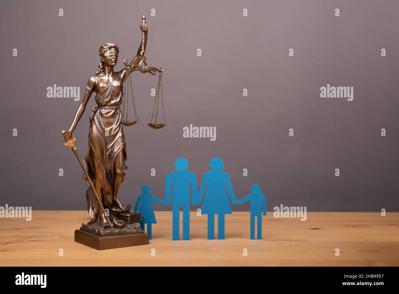 Statua di una donna con scale come simbolo di legge su una superficie di legno con silhouette di una famiglia Foto Stock Statua di una donna con scale come simbolo di legge su una superficie di legno con silhouette di una famiglia Foto Stock