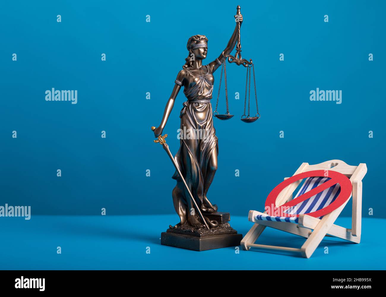 Statua di una donna con le scale come simbolo di legge e giustizia su una superficie blu con un segno di stop Foto Stock Statua di una donna con le scale come simbolo di legge e giustizia su una superficie blu con un segno di stop Foto Stock