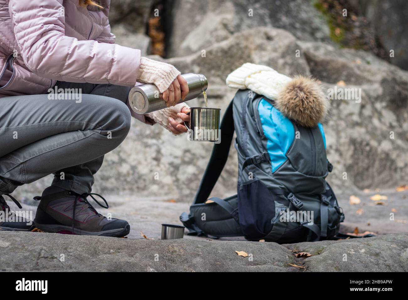 La donna versa una bevanda calda dai thermos in una tazza di metallo durante l'escursione autunnale. Rinfresco in montagna. Backpacker in natura Foto Stock