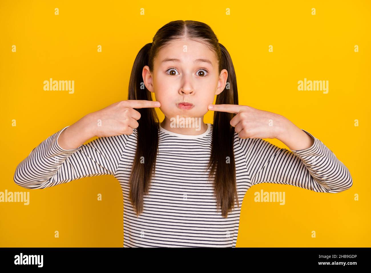 Foto di giovane scuola ragazza tenere respiro foling punto dita guance isolate su sfondo giallo Foto Stock