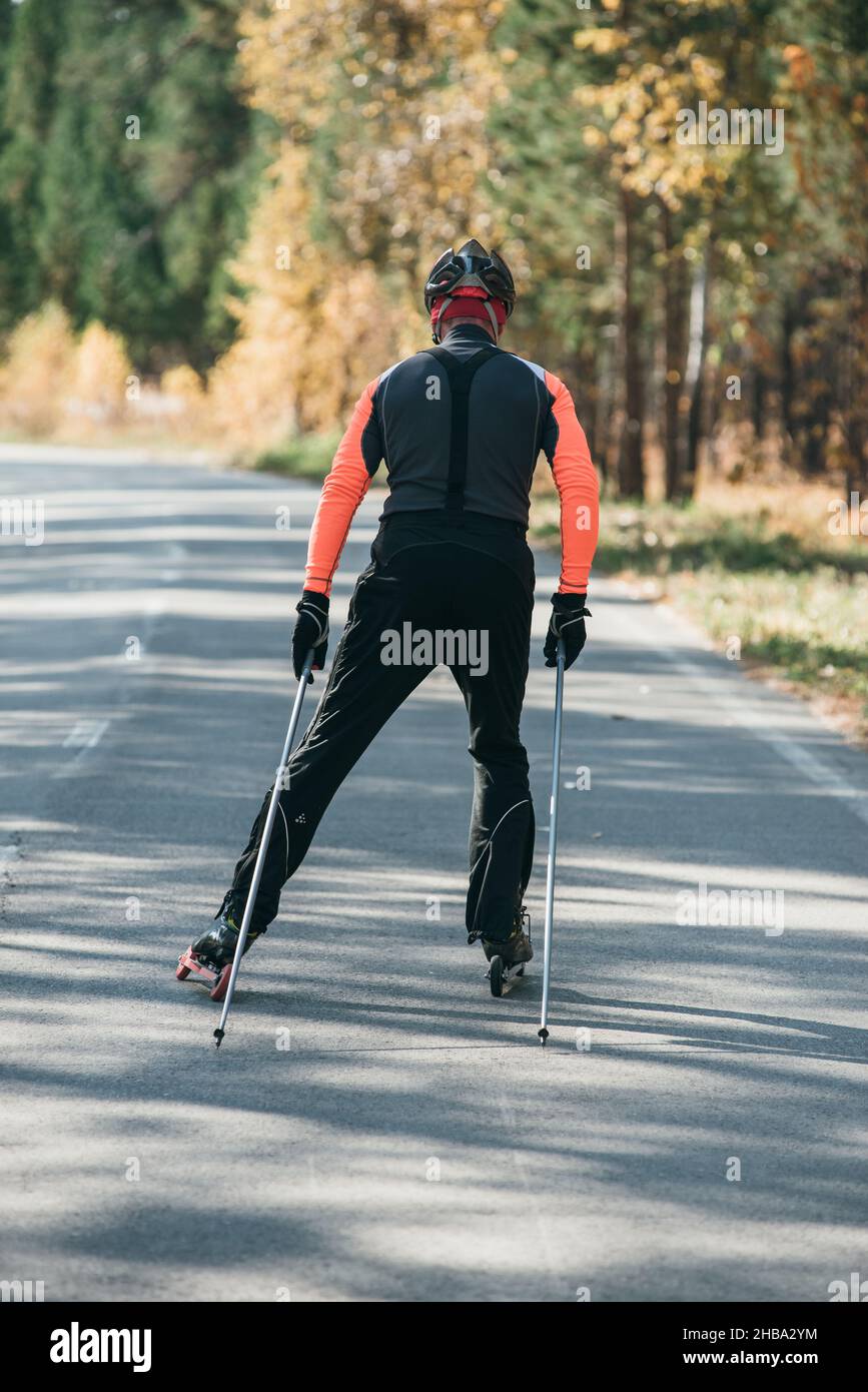 La formazione di un atleta sul rullo pattinatori. Il biathlon ride sul rullo di sci con bastoncini da sci, nel casco. Allenamento di autunno. Sport a rullo. Foto Stock