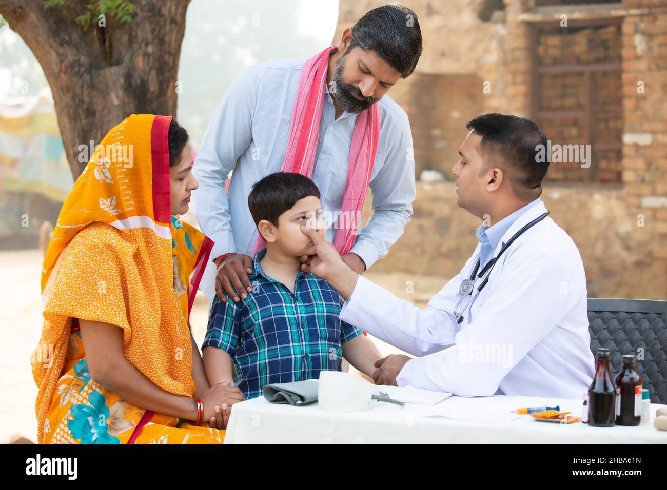Medico indiano esaminare bambino piccolo paziente in villaggio, donna che indossa sari con suo marito e figlio consulenza medica persona, Rural India sanità Foto Stock