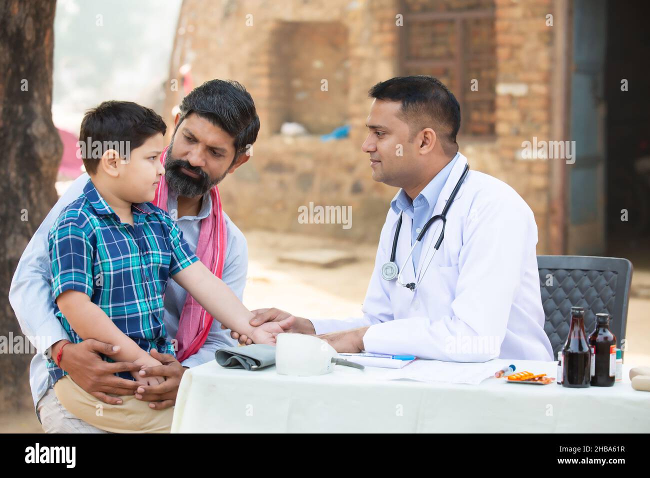 Medico indiano esaminare bambino piccolo paziente in villaggio, Padre con suo figlio consulente medico persona, Rural India campo sanitario concetto. Foto Stock