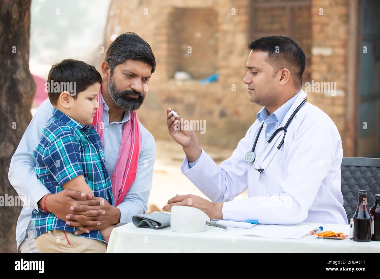 Medico indiano esaminare la febbre del paziente del bambino piccolo al villaggio con termometro digitale, Padre con il suo figlio che consulta la persona medica, Rural India guarire Foto Stock