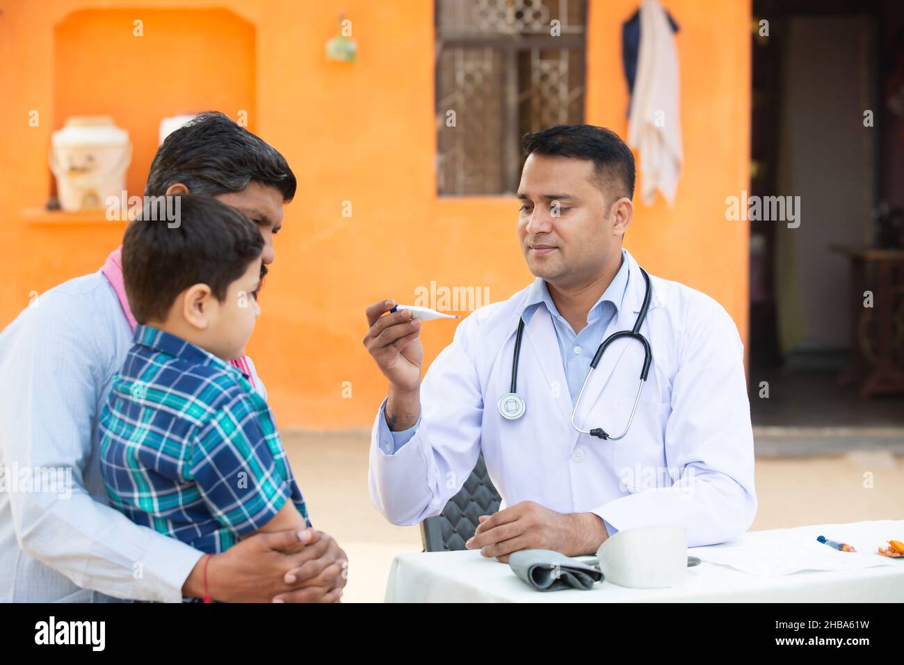 Medico indiano esaminare la febbre del paziente del bambino piccolo al villaggio con termometro digitale, Padre con il suo figlio che consulta la persona medica, Rural India guarire Foto Stock
