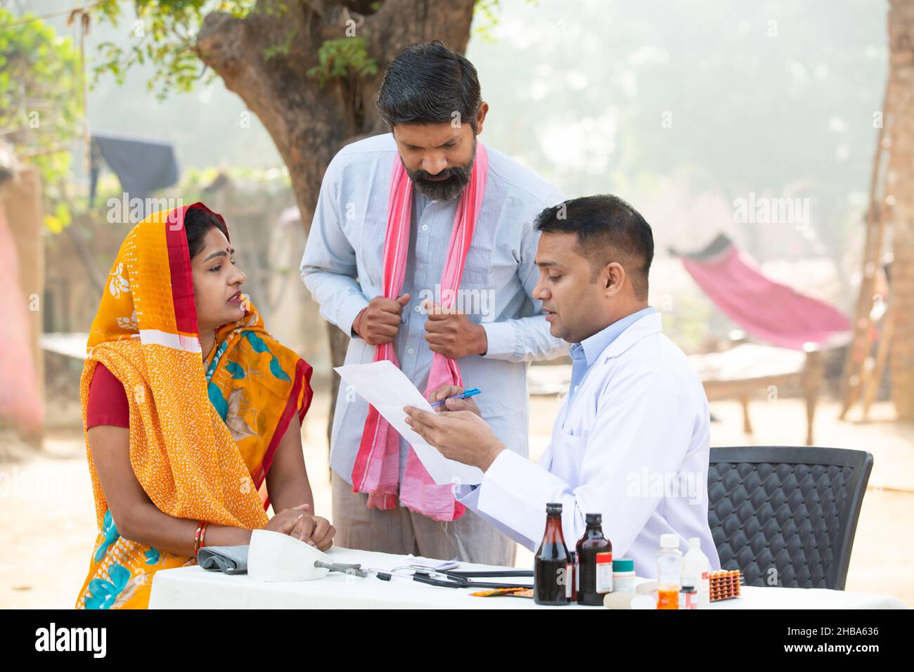 Medico indiano che spiega il test medico o prescrivere la medicina al paziente in villaggio, donna che indossa sari con suo marito che ottiene l'esame da medica Foto Stock
