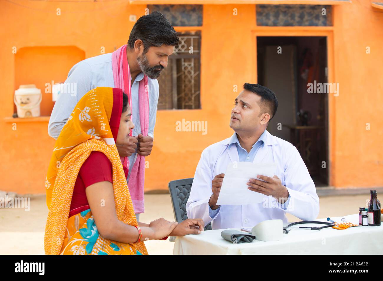 Medico indiano che spiega il test medico o prescrivere la medicina al paziente in villaggio, donna che indossa sari con suo marito che ottiene l'esame da medica Foto Stock