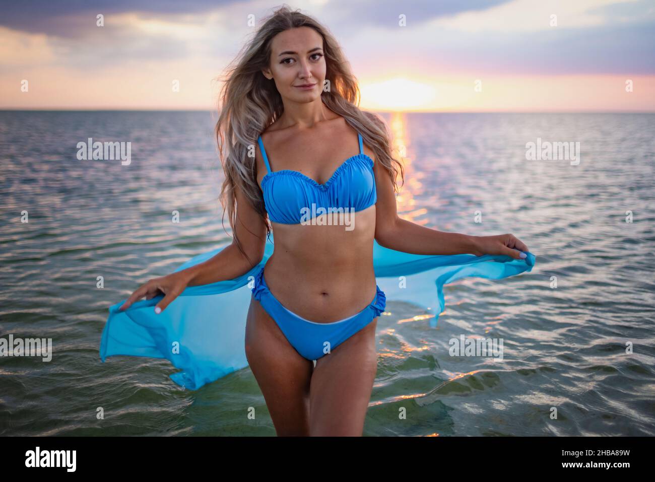 Una ragazza in un costume da bagno blu e un pareo luminoso che si posa  sullo sfondo di un tramonto in estuario con acqua trasparente Foto stock -  Alamy