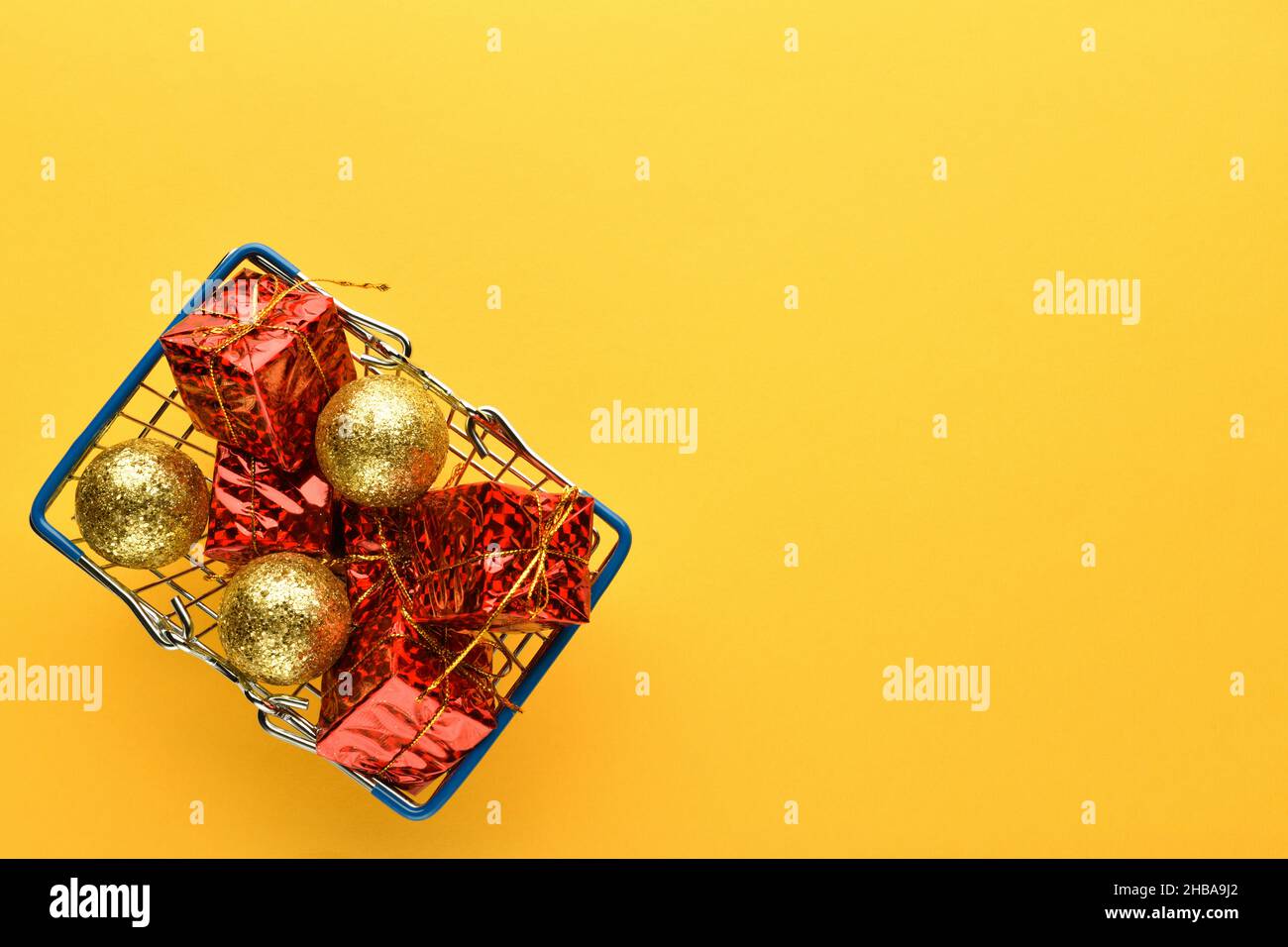 Regali e giocattoli di Natale in un cestino su sfondo giallo chiaro, spazio vuoto per il testo sulla destra. Nuovo anno e sfondo di Natale. Foto Stock