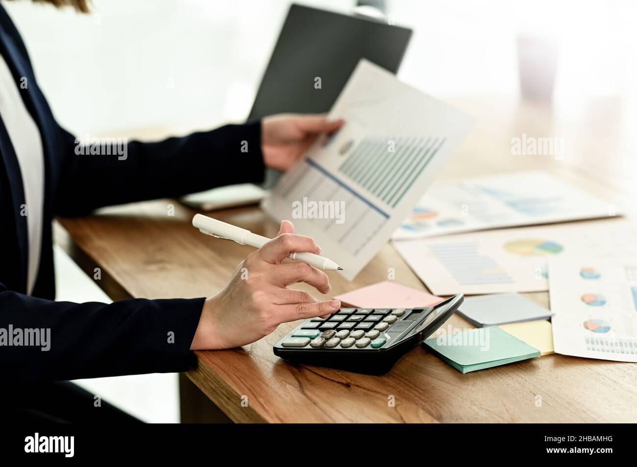 Una donna d'affari che usa una calcolatrice e tiene un grafico, una donna che tiene un grafico in mano usando una calcolatrice, una giovane donna che analizza i grafici di dati wi Foto Stock
