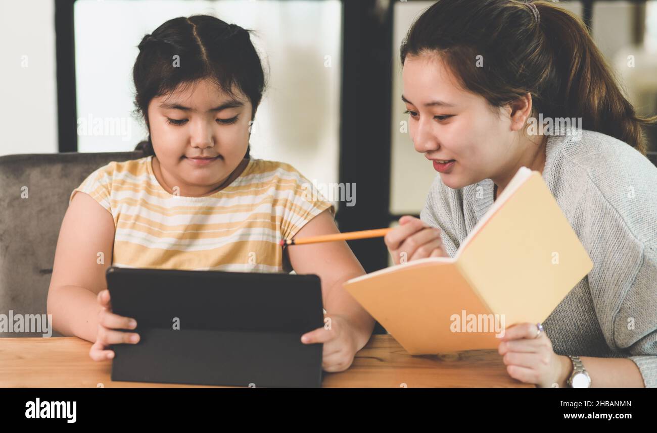 Una bambina sta studiando con il suo insegnante a casa, ragazze adolescenti che insegnano lavoro a casa alle ragazze, Una bambina sta studiando duro con un tablet e lei Foto Stock