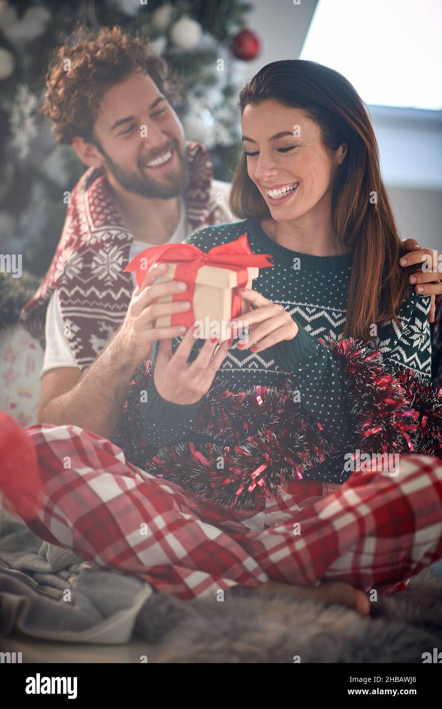 Un ragazzo sta dando un regalo di natale alla sua ragazza amico mentre sono seduti sul pavimento in una piacevole atmosfera a casa insieme. Natale, casa, Foto Stock