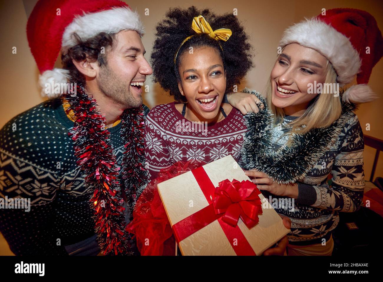 Un gruppo di amici allegri tiene un regalo e posa per una foto durante una festa di Capodanno in un'atmosfera festosa a casa. Natale, Capodanno, Foto Stock