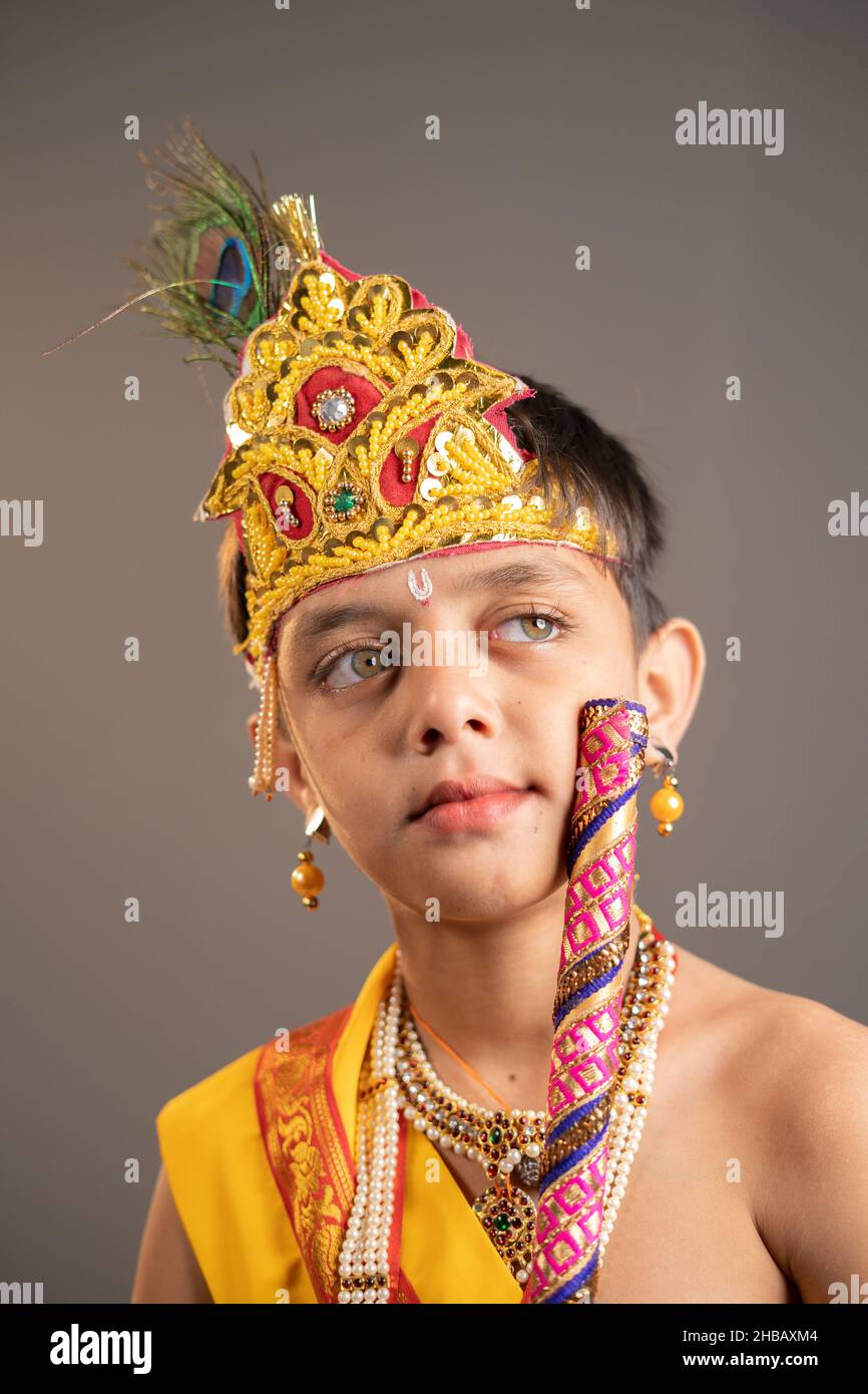 Piccolo Krishna pensando tenendo il flauto in mano su sfondo grigio durante shri krishna Janmashtami. Foto Stock