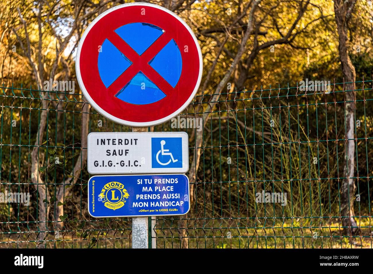 Due segnali stradali impilati segnano un posto auto per disabili vicino a Bormes-les-Mimosas, dipartimento di Var, Francia: un cartello di divieto di sosta con l'aggiunta "Interdit sauf G.I.G.-G.I.C." e un cartello donato dal Lions Club che fa appello, "Se prendi il mio posto, prendi anche la mia disabilità." Foto Stock