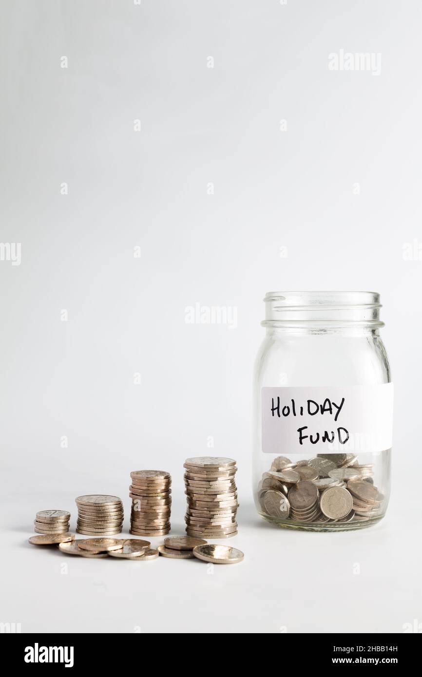 Concetto di risparmio di denaro per una vacanza e crescente valore nel tempo, mucchi di monete d'argento che compounding e crescere accanto ad un vaso con monete in h etichettato Foto Stock