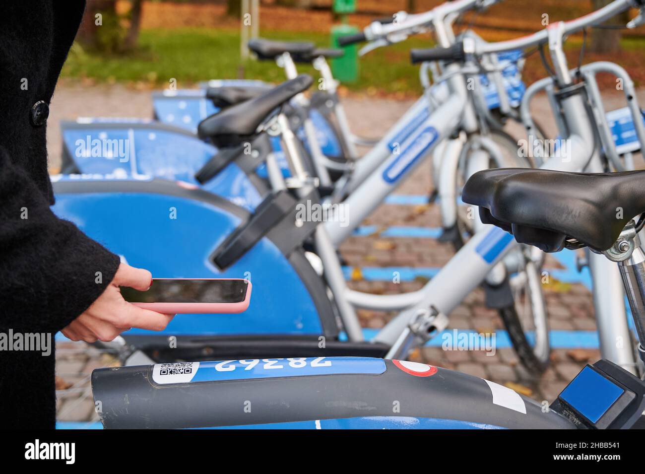 Primo piano di scansione femminile codice QR con telefono cellulare mentre si paga il noleggio biciclette sulla strada. Giovane donna che utilizza il servizio di noleggio biciclette urbano. Foto Stock