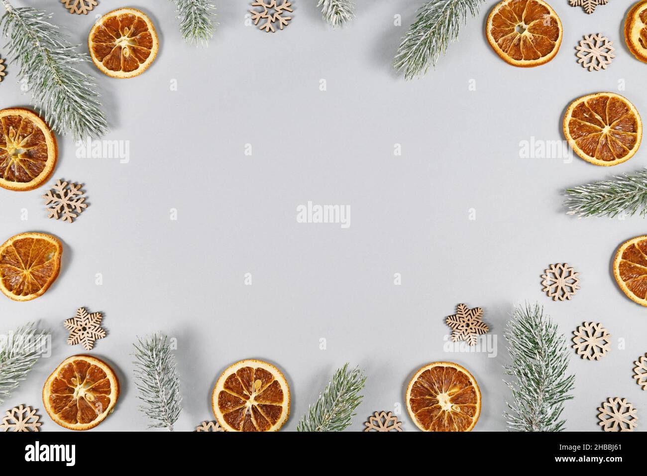 Cornice con rami di abete invernale, fette di arancio secco e fiocchi di neve su sfondo grigio con spazio copia Foto Stock