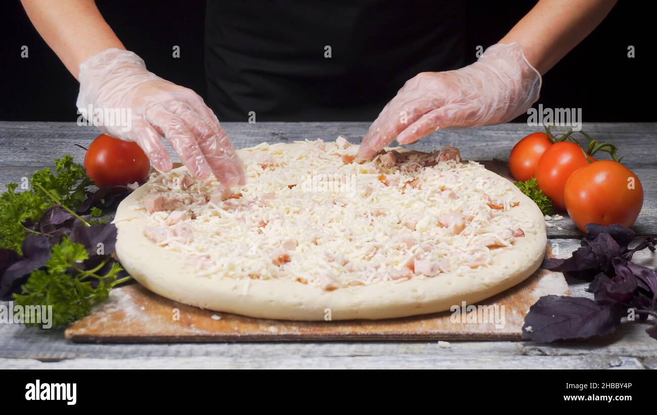 Primo piano per cucinare mani in guanti preparazione pizza sdraiato su  tavola di legno con verdure fresche, concetto di foodporn. Lo chef prepara  la pizza al tavolo su Bla Foto stock 