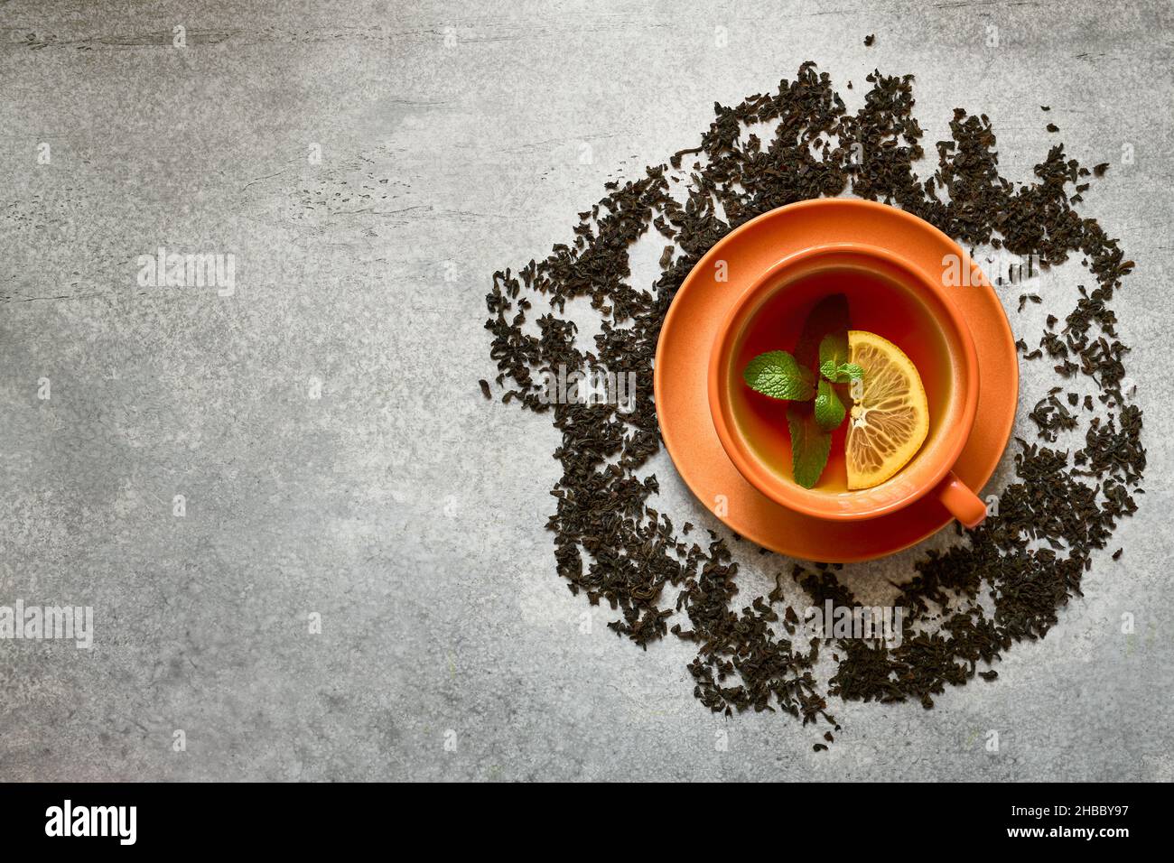 Tazza di tè in ceramica arancione con foglia di menta e fetta di limone su sfondo grigio di cemento con spazio copia, vista dall'alto Foto Stock
