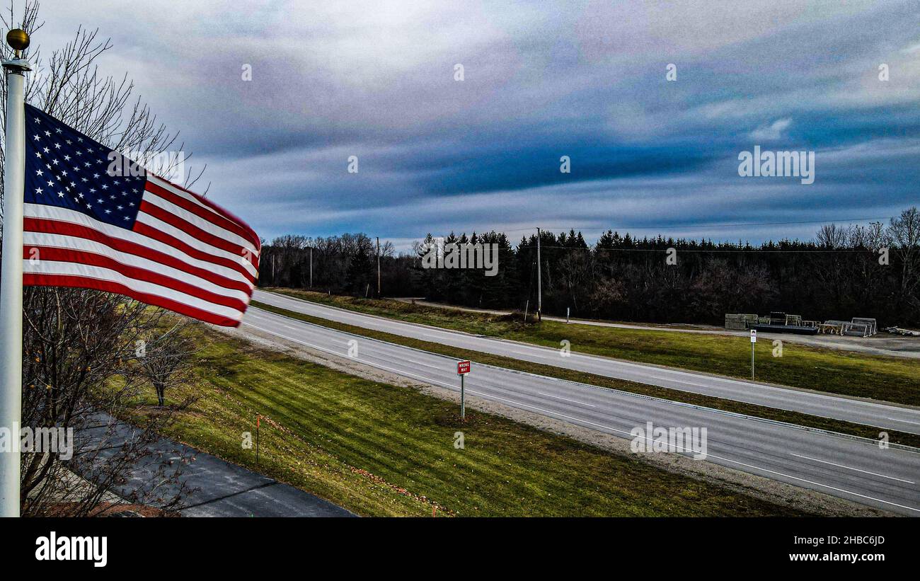 US Flag scorre nel vento con un cielo moody sopra durante l'autunno. Strada di campagna sullo sfondo con alberi. Novembre 2021 Foto Stock