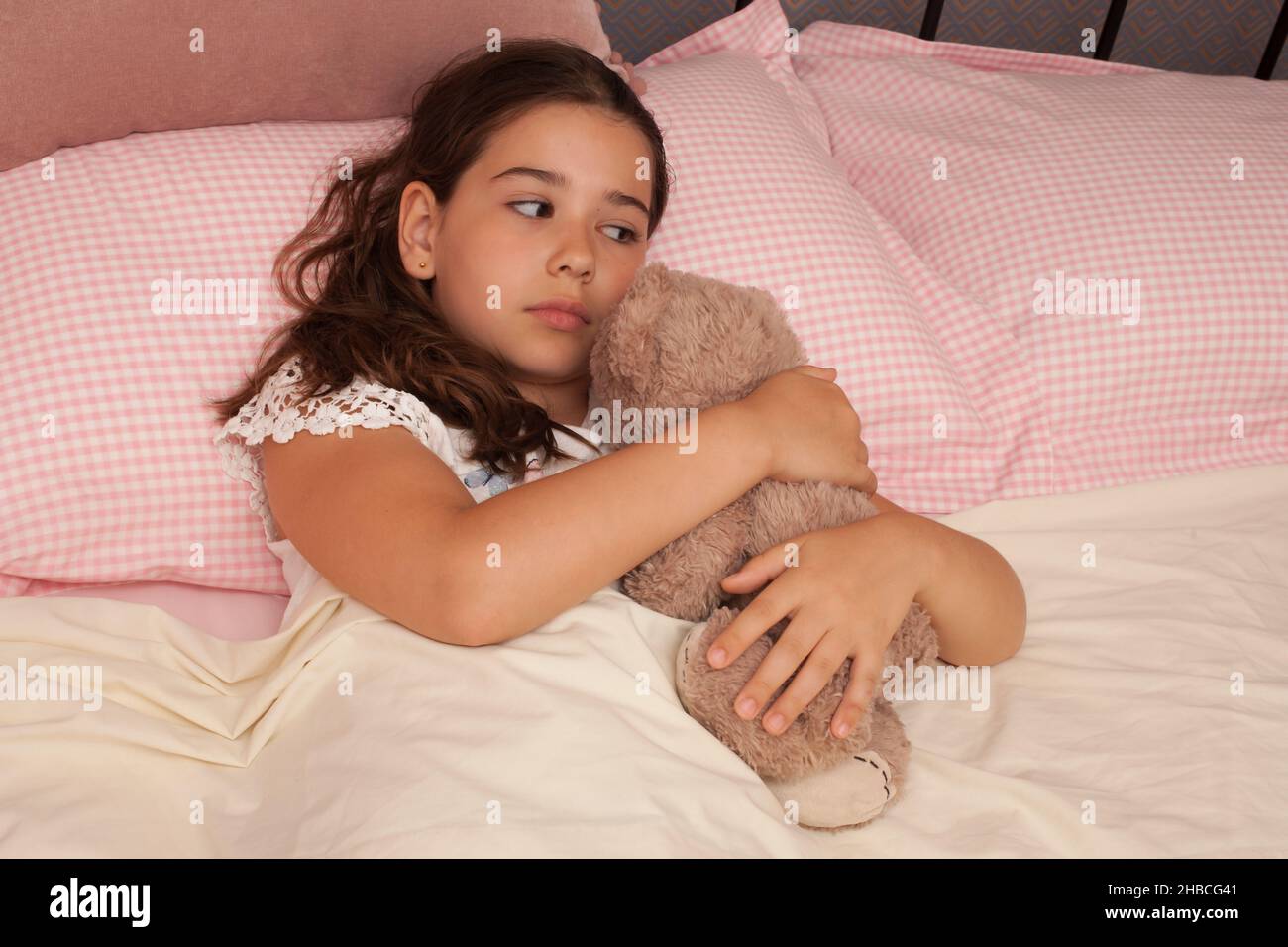 Una ragazza nel suo letto che guarda triste coccolare il suo orsetto, preso il 13 agosto in lana, Dorset, Regno Unito Foto Stock
