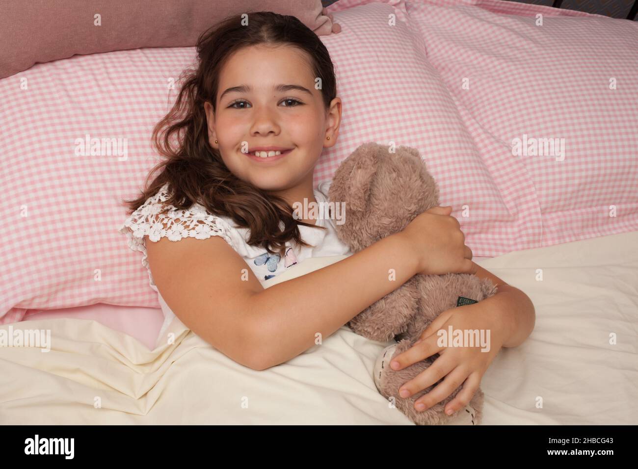 Una ragazza felice nel suo letto coccolando il suo orsacchiotto, preso il 13 agosto in lana, Dorset, Regno Unito Foto Stock