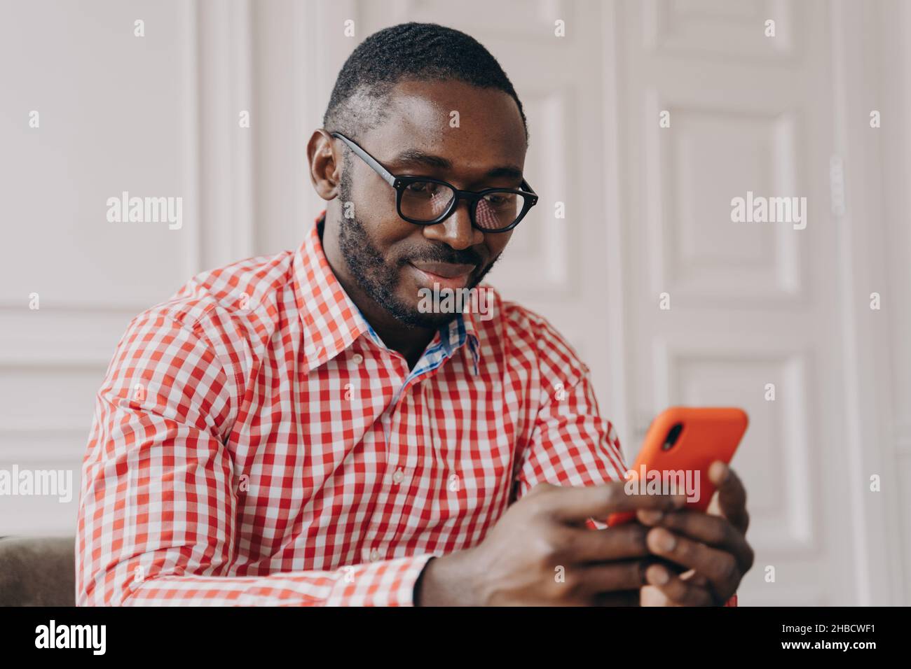 Allegro uomo biraciale millenario con smartphone, seduto alla scrivania Foto Stock