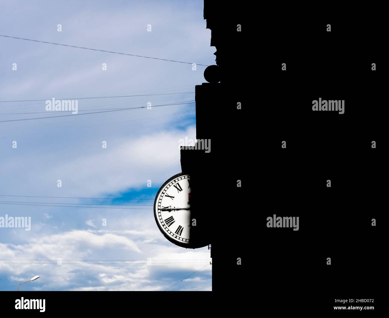 Orologio 24 ore sull'edificio con metà del quadrante in ombra da casa contro il cielo nuvoloso. Orologio mano a 45 minuti. Concetto - copertina del libro, copertina dell'album. Foto Stock