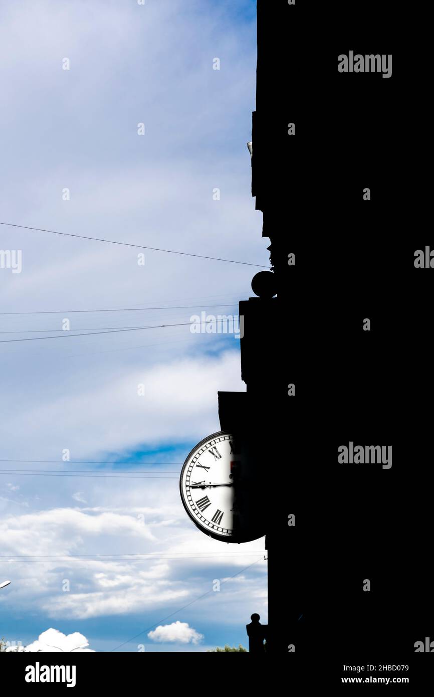 Orologio 24 ore sull'edificio con metà del quadrante in ombra da casa contro il cielo nuvoloso. Orologio mano a 45 minuti. Concetto - copertina del libro, copertina dell'album. Foto Stock