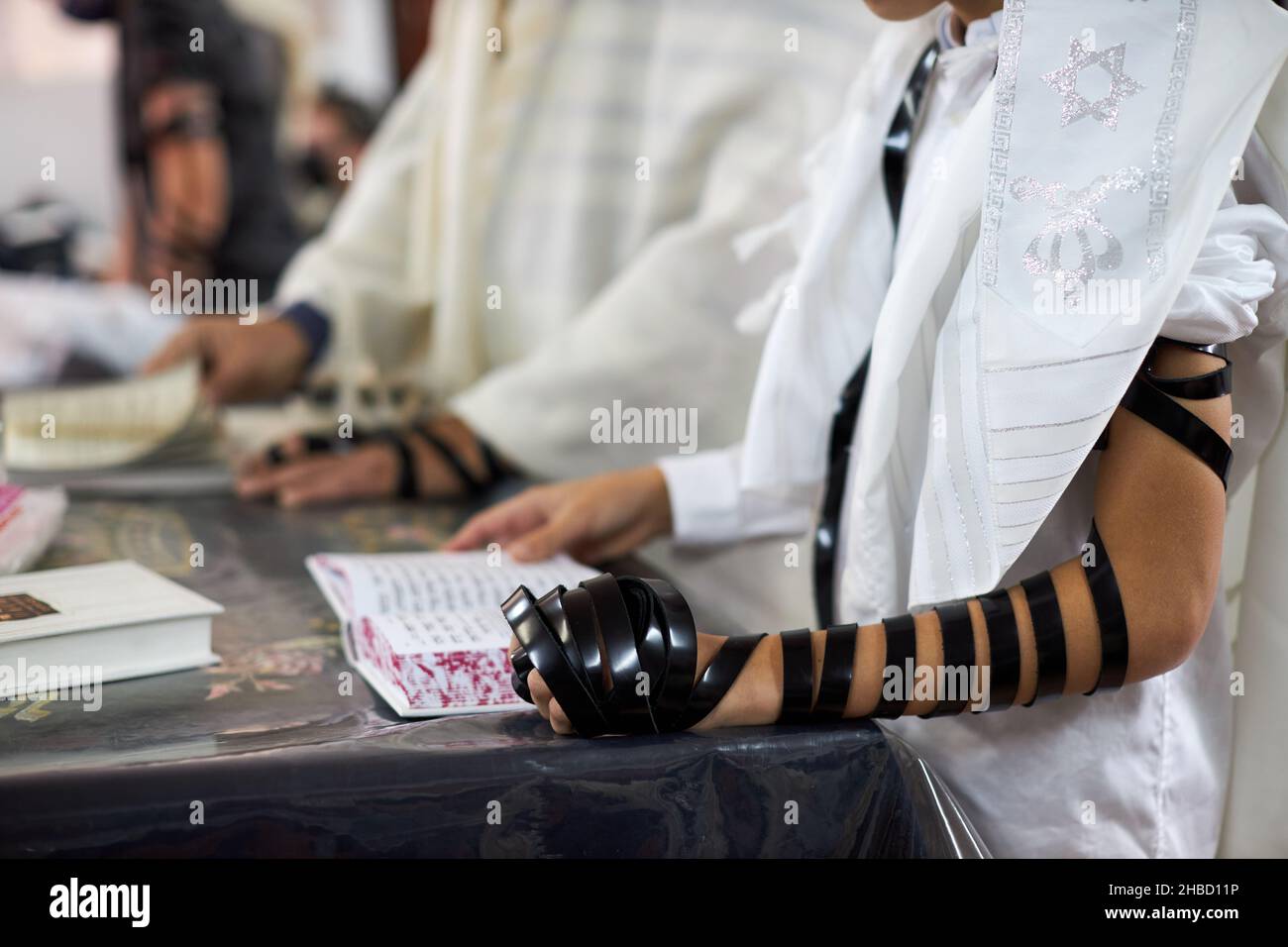 Primo piano, giovani uomini che leggono la preghiera ebraica e una mano con tefillin e talit.Selective focus Foto Stock