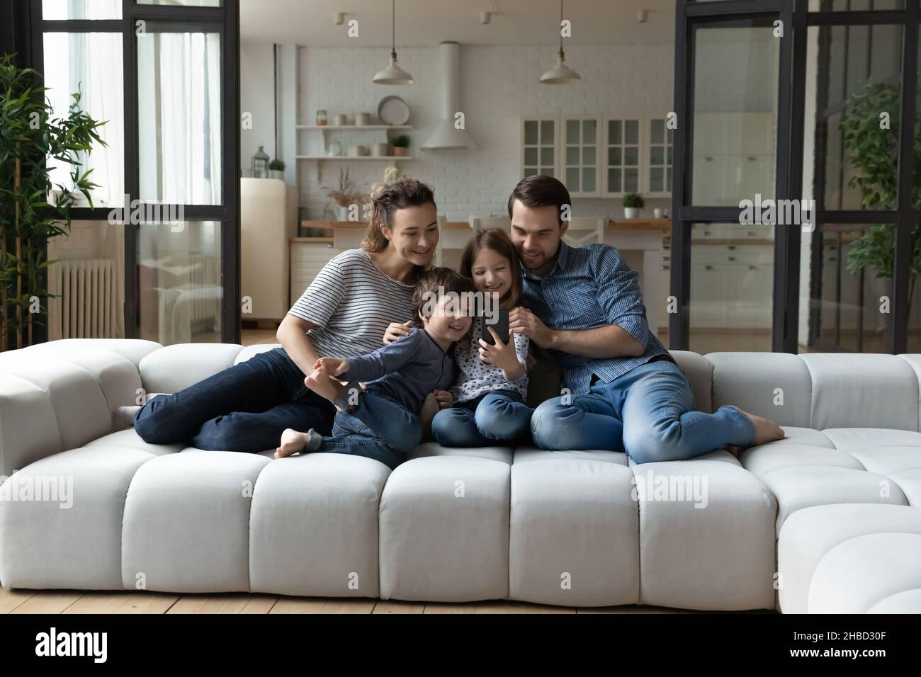 Famiglia felice con i bambini che usano lo smartphone, seduti sul divano insieme Foto Stock