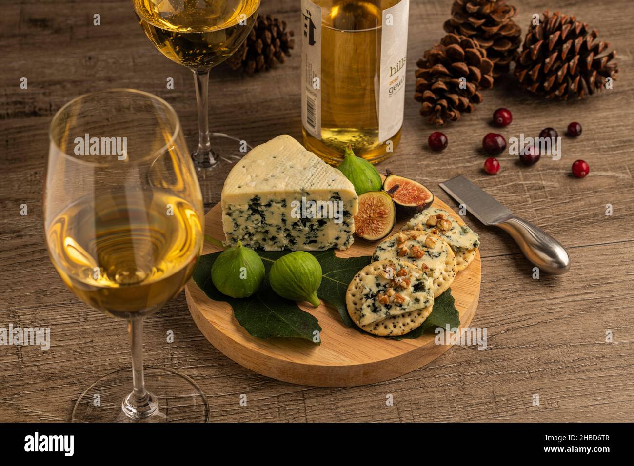Degustazione di vini bianchi e formaggi natalizi con formaggio blu, cracker e fichi su un tavolo di legno, pineconi e mirtilli raffigurati come guarnitura Foto Stock