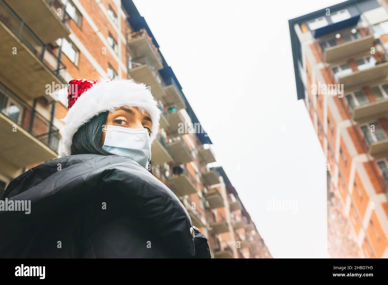 Donna si alza con cappello di Natale in strada circondata da case di blocco. Vacanze di istmas di auto. Foto Stock