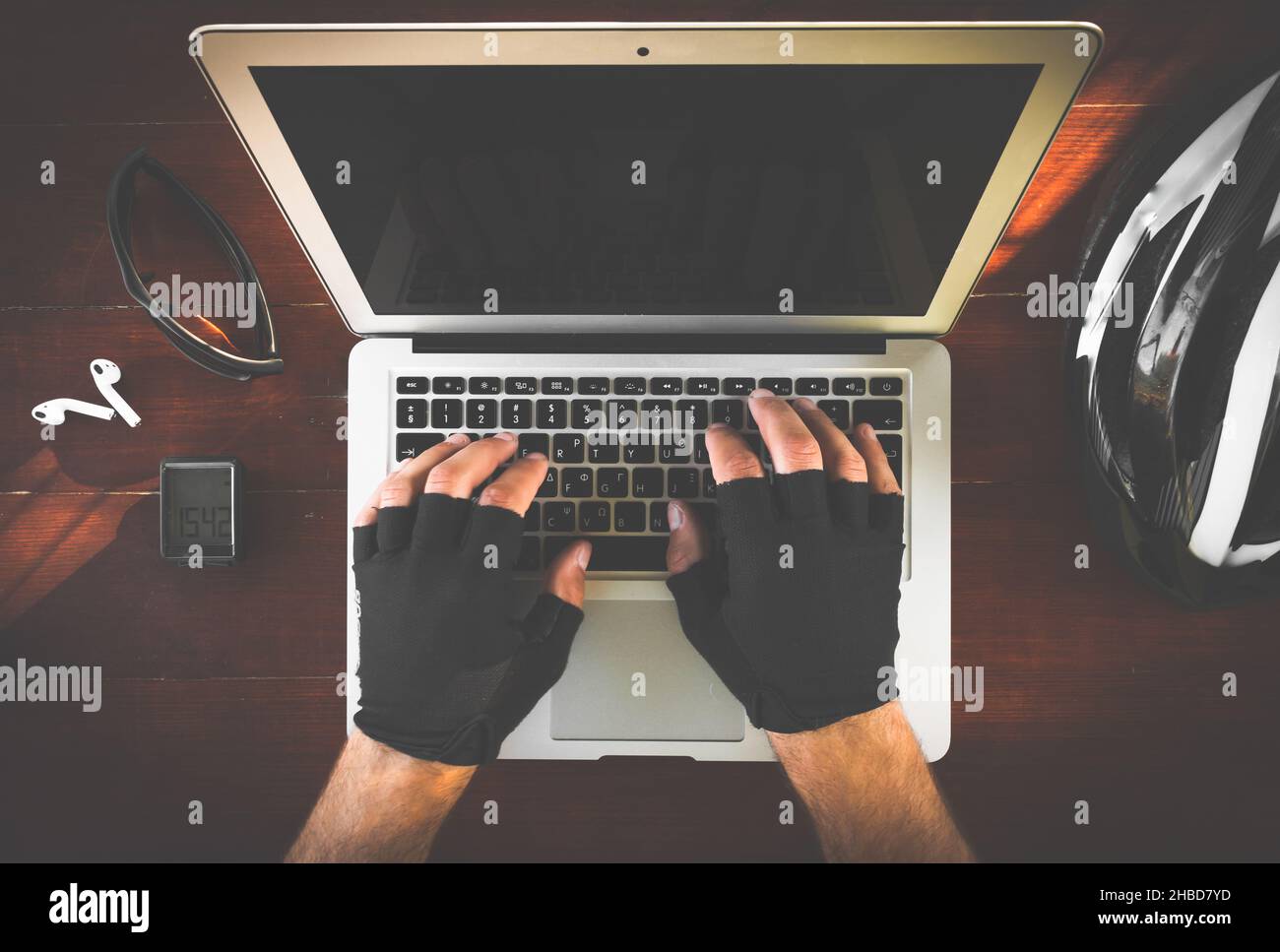 Due mani con guanti stanno digitando sulla tastiera del portatile laptop con accessori da ciclismo (casco, computer da bicicletta, auricolari, occhiali) led sul Foto Stock