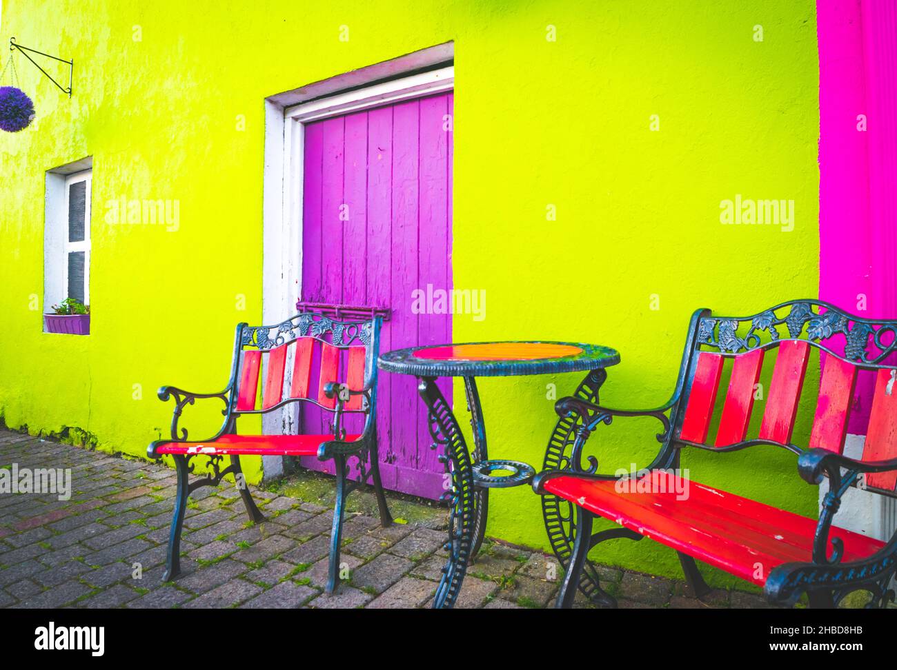 Terrazza colorata allestita con sedie in stile retrò; tavolo e parete verde, porte d'ingresso viola Foto Stock