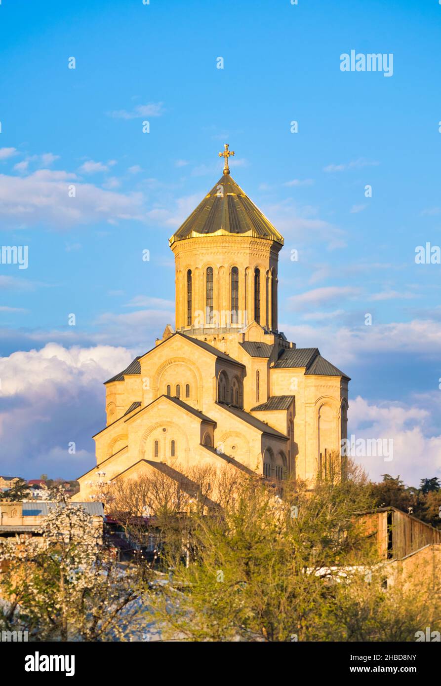 Chiesa della santa trinità Orthodox a Tbilisi con molti hosues intorno e alberi di primavera in fiore. Religione e cultura di Kartveliani. Sakartvelo. Foto Stock