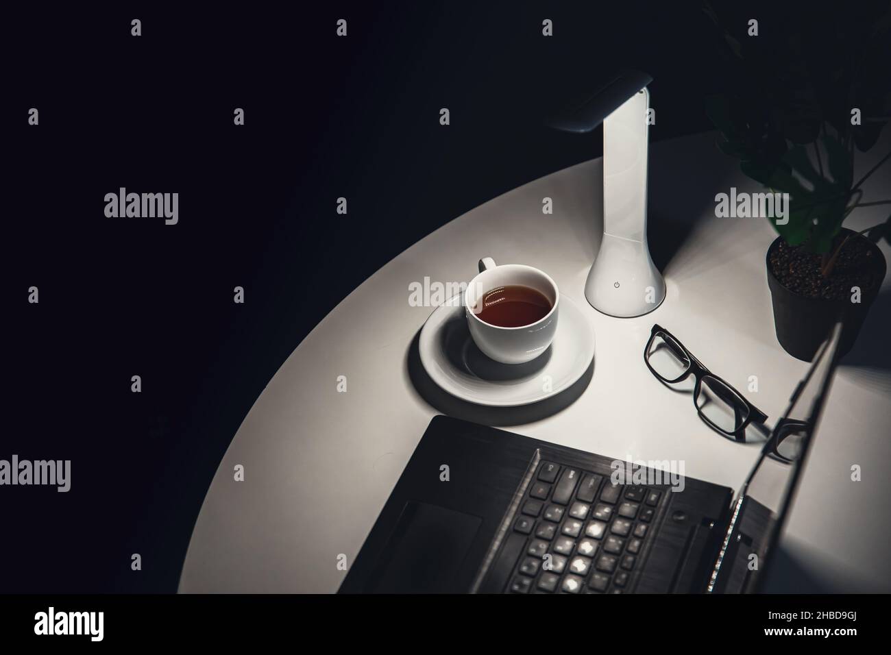 Tazza di tè, lampada e laptop sulla scrivania di notte. Foto Stock